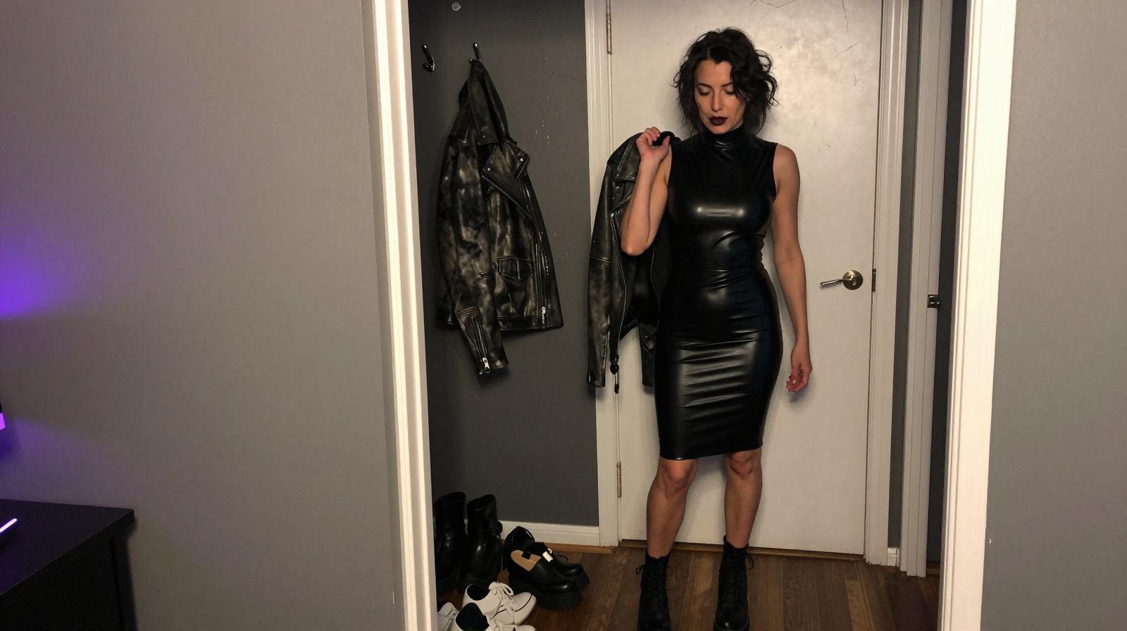 Woman in a black latex dress and boots getting ready at home with a leather jacket